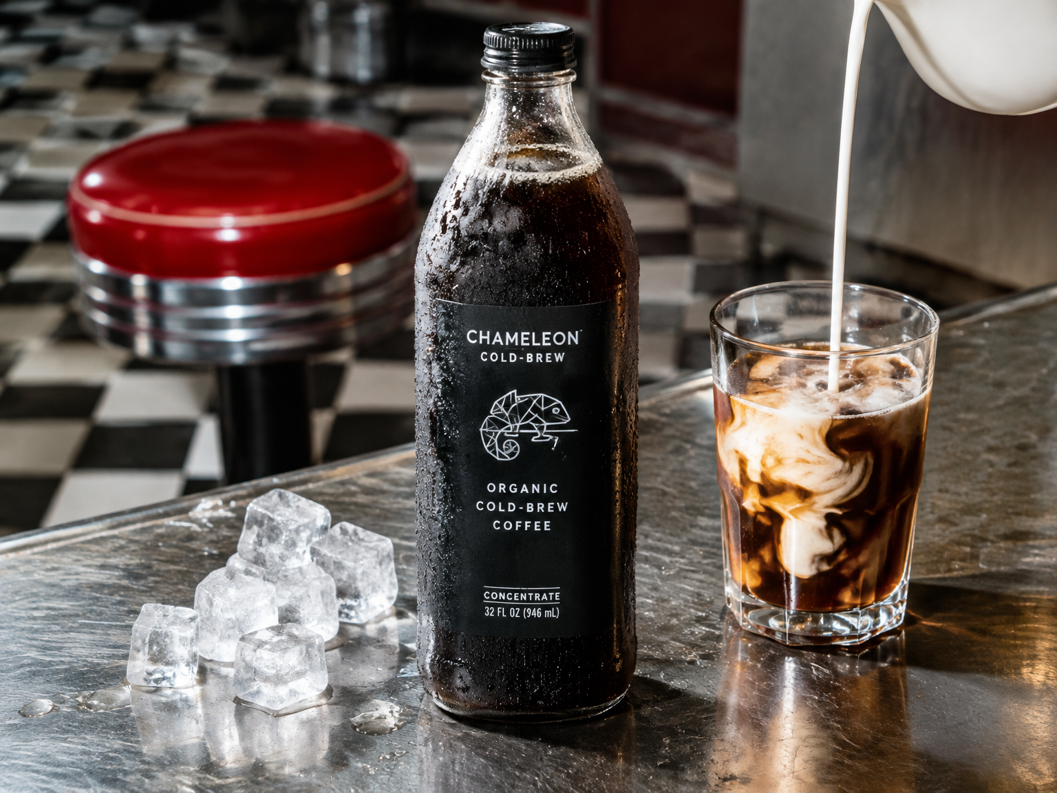 Glass bottle of cold brew beaded with condensation on a chrome diner counter beside an iced coffee