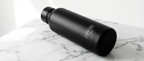 Black insulated water bottle placed on marble surface in minimal product photography style